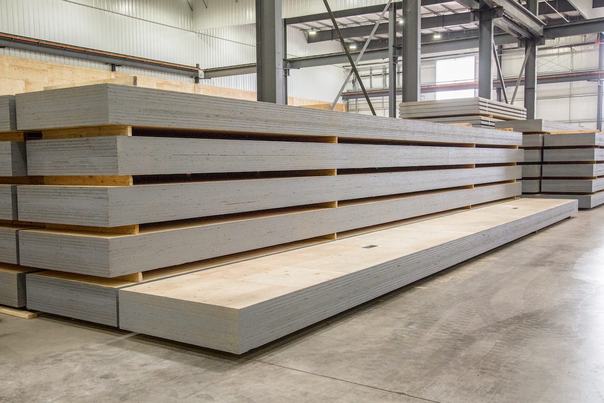 Stacks of large, laminated wooden panels—Mass Ply Panel, which received patents and passed fire safety testing—fill a warehouse with concrete floors and high ceilings.